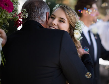 A father hugs the bride as the groom stands in the background